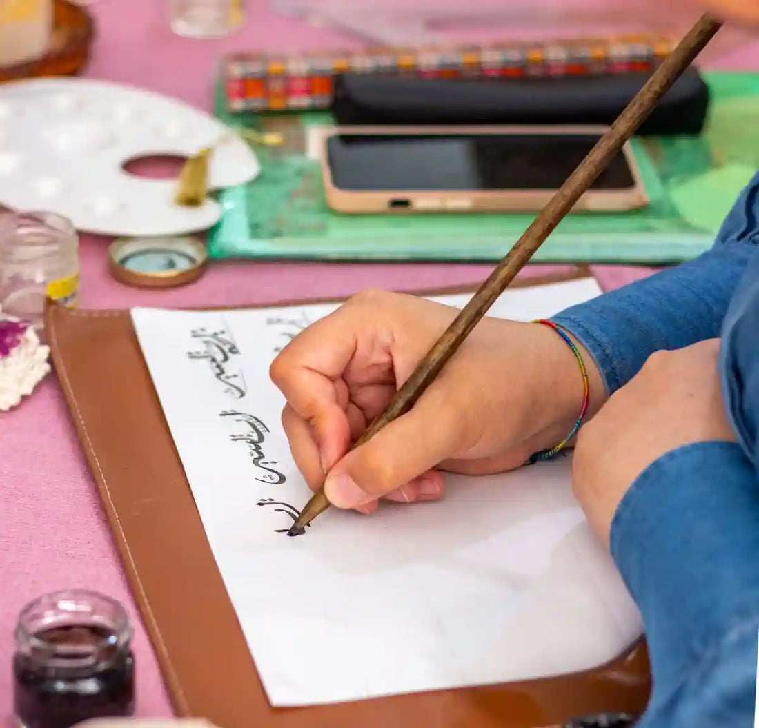 [ Image1: Hands practicing traditional Arabic calligraphy on paper.]